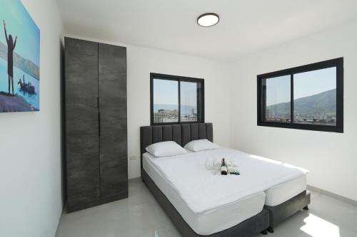 a white bedroom with a large bed and two windows at לוי-קיישן מגוון דירות גן ופנטהאוזים וסוויטות נוף ברחוב הצנחנים in Tiberias