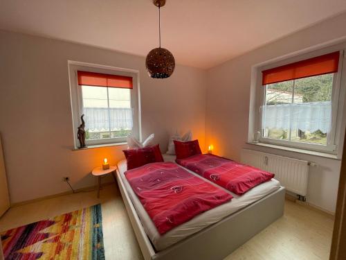 een slaapkamer met een bed met rode lakens en 2 ramen bij Ferienwohnung Am Wald in Großschönau