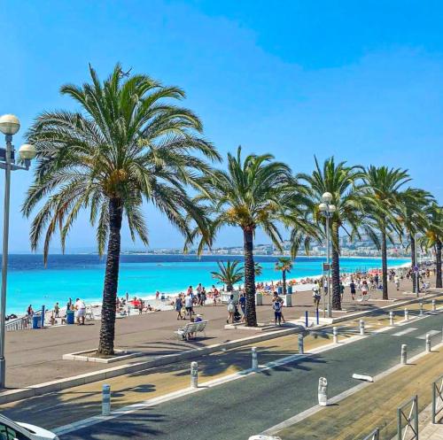 des personnes se promenant sur une plage avec des palmiers et l'océan dans l'établissement Design Apartment near the Beaches of Nice, à Nice