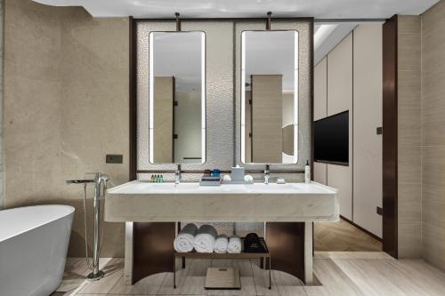 a bathroom with a sink and a tub and mirror at Wanda Jin Hotel Ordos in Ordos