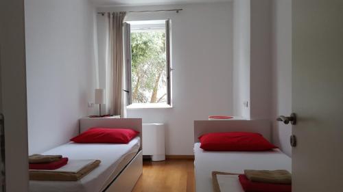 two beds with red pillows in a room with a window at Apartments Laus in Dubrovnik
