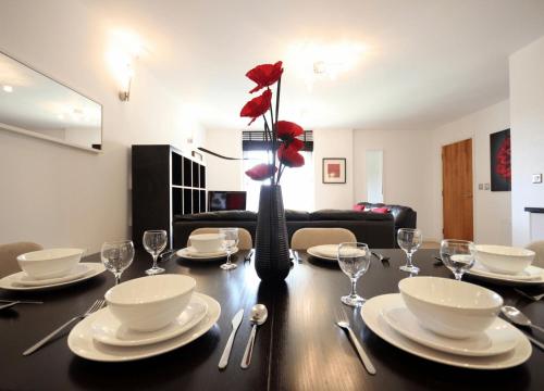 a dining room table with a vase with red flowers on it at Reading Modern Two Bedroom Apartment in Reading