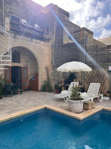 a pool with two chairs and an umbrella at Arkati house in Munxar