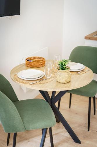 une table en bois avec des assiettes, des verres et des chaises vertes dans l'établissement Stud Aloé 2pers wifi city center, à Cambrai