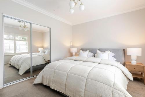 ein weißes Schlafzimmer mit einem großen Bett und einem Spiegel in der Unterkunft Adelaide Oval Townhouse - Walk to the AFL & CBD in North Adelaide