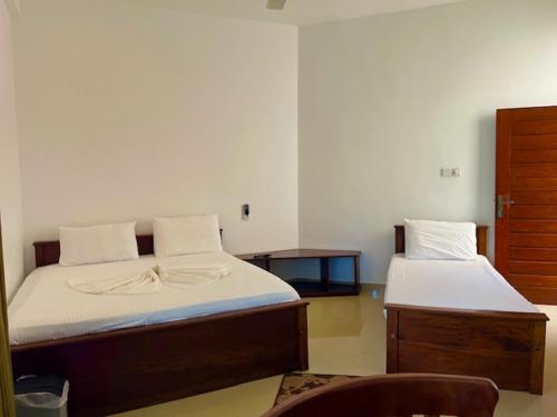 a bedroom with two beds with white sheets and a chair at Kamatha Hotel & Restaurant in Ambalantota