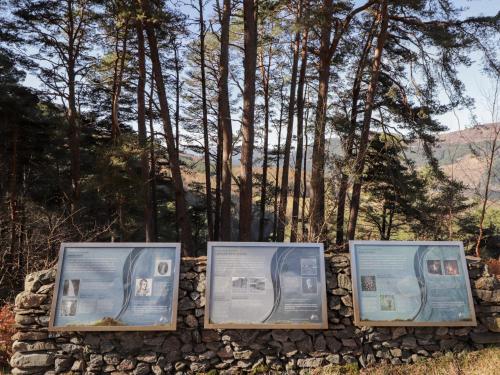 a stone wall with signs on it in front of trees at Faodail Glenlia in Foyers