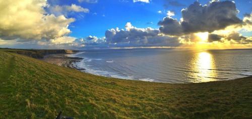 a view of the ocean from a grassy hill with the sunset at Cozy & Contemporary Lodge by the woods in Cowbridge