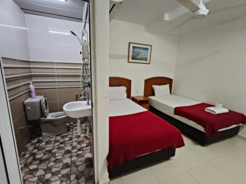 a room with two beds and a sink and a bathroom at Kota Lodge Guest House in Melaka