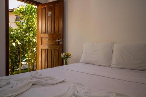a bed with white sheets and a wooden door at Alto do Aeroporto Hotel in Porto Seguro