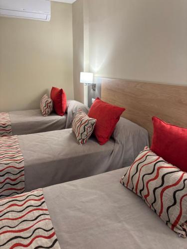 three beds in a room with red pillows on them at Hotel Estilo MB - Mar del Plata in Mar del Plata