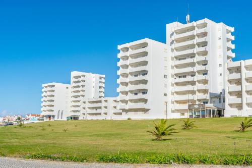 two white apartment buildings on a grassy hill next to a road at Baleal Blue Sky in Ferrel