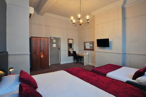 バッキンガムにあるThe White Hart Inn by Greene King Innsのベッド2台とデスクが備わるホテルルームです。