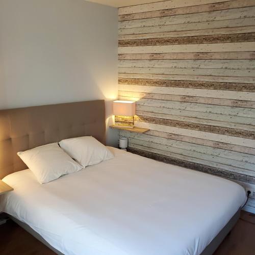 une chambre avec un lit blanc et un mur en bois dans l'établissement Cosy Flat - Terrasse - Parking - 40m2, à La Rochelle