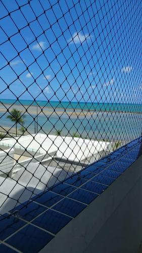 a view of a beach through a wire fence at Flat beira mar, Olinda 4 Rodas 309 in Olinda