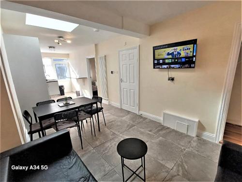Una sala de estar con una mesa y un televisor en la pared. en Spacious 5 bedroom House - 10min walk to Becrontree Station, en Dagenham