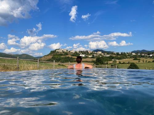 a person in a infinity pool with a castle in the background at Agriturismo Casale Montebello in Monteleone di Spoleto
