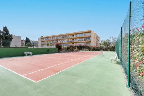 un court de tennis en face d'un bâtiment dans l'établissement Studio neuf bord de mer Le Lavandou - Piscine - Tennis - Boulodrome dans la résidence, au Lavandou
