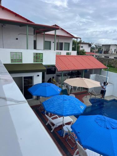 eine Terrasse mit blauen Sonnenschirmen und Stühlen sowie einem Pool in der Unterkunft Hostal Canuto Inn in Ayangue