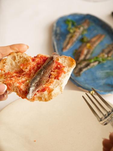 a person holding a slice of pizza with a fish on it at Hostal Empúries in L'Escala
