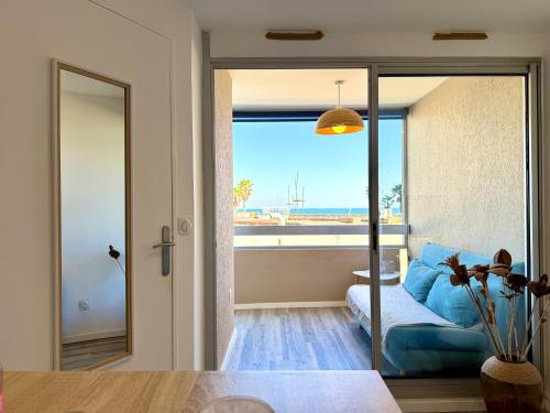 un salon avec un canapé bleu et une grande fenêtre dans l'établissement Le Maëva - T2- Front de mer- Clim - Parking - Wifi- SudSéjourConciergerie, à Canet