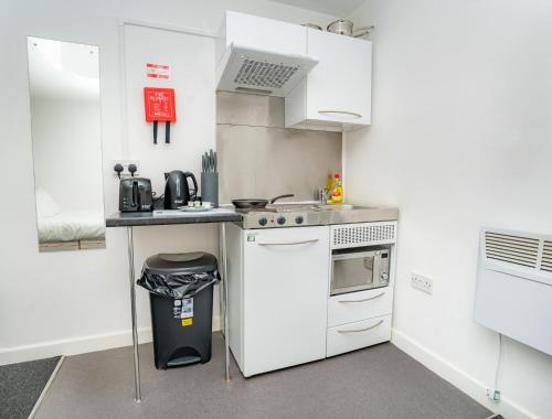 a small kitchen with white appliances and a trash can at Compact & Cosy Central Coventry Budget Studio in Coventry