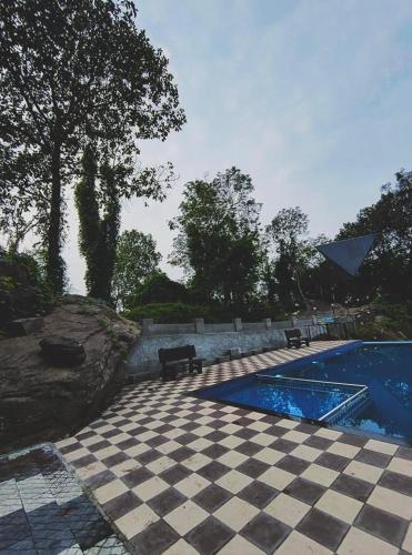 a swimming pool with two benches and a checkered floor at Private Hut in Thusharagiri in Vallikavungal