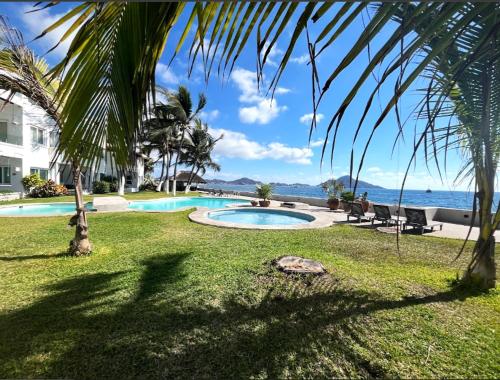 a swimming pool with a palm tree and the ocean at Penthouse en Manzanillo a Pie de Playa in Manzanillo