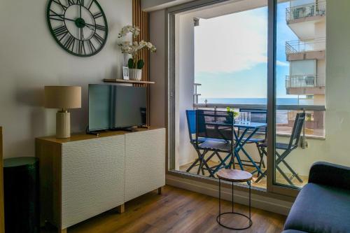 - un salon avec une télévision, une table et une horloge dans l'établissement Bel appartement vue mer - quartier des Présidents - 5 personnes, à Les Sables-dʼOlonne