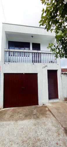 a white house with a red garage door and a balcony at Quarto em apartamento próximo ao aeroporto in São José dos Pinhais