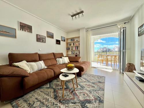 a living room with a brown couch and a table at Stunning frontline apartment with golf views and pool in Sucina