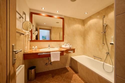 a bathroom with a tub and a sink and a mirror at Landhotel Schermer in Westendorf