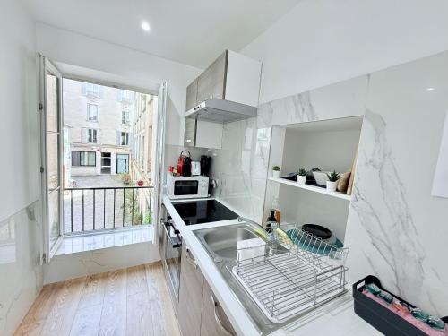 une cuisine blanche avec un évier et une fenêtre dans l'établissement Refait à Neuf 2 pièces - Paris - tout équipé - Parking, à Paris