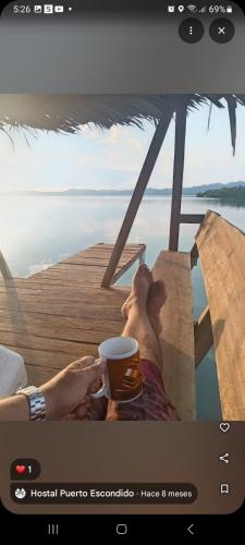 a person sitting on a pier with a cup of coffee at Hostal Puerto Escondido in Bocas del Toro