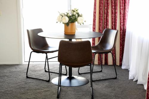 a table with three chairs and a vase of flowers on it at Sunny Villa Guest House in Auckland