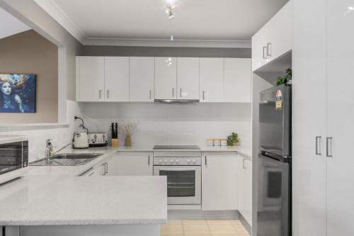 a kitchen with white cabinets and a stainless steel refrigerator at Mermaids at the Bay in Toowoon Bay