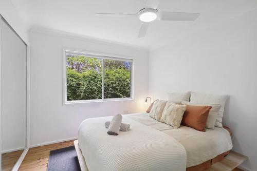 a white bedroom with a bed and a window at Cosy Creekside in Dora Creek