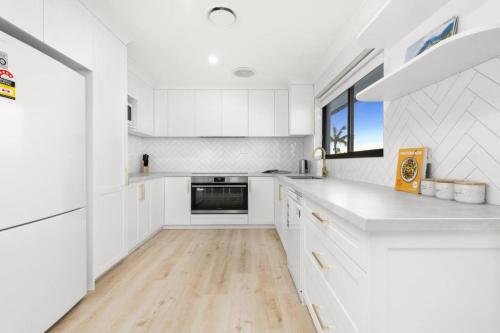 a white kitchen with white cabinets and a wooden floor at Coastal Oasis in Toukley