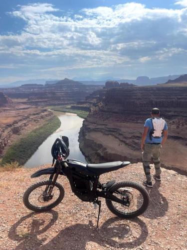 a man standing next to a motorcycle on top of a canyon at The Caves at Moab - At Private Riverside Ranch in Moab
