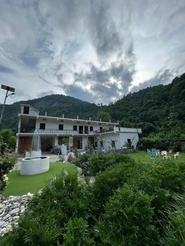 a large white building with a hill in the background at Lamyali Farm in Rishīkesh