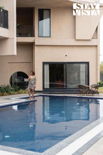 a woman is standing next to a swimming pool at StayVista at Urban Escape - 2 Pools, Lawn & WiFi in Jaipur
