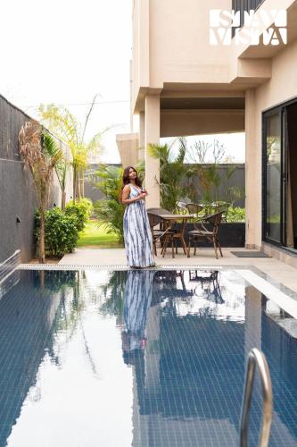 a woman is standing next to a swimming pool at StayVista at Urban Escape - 2 Pools, Lawn & WiFi in Jaipur