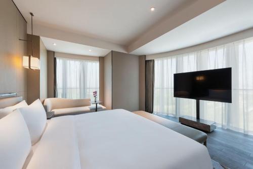 a bedroom with a large white bed and a tv at Grand Mercure Shanghai Lingang in Shanghai