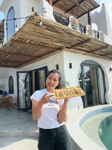 a woman holding up a tray of food in front of a house at Santa Fe House - Gành Đá Đĩa in Phú Hạnh (5)