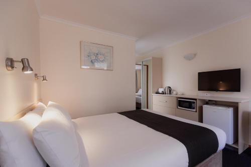 a hotel room with a white bed and a flat screen tv at Argyle Motor Lodge in Hobart