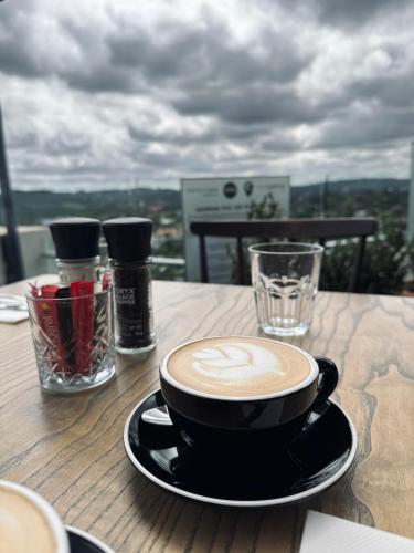 a cup of coffee sitting on a wooden table at The Capital Trilogy Menlyn Maine in Pretoria