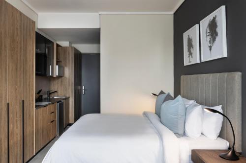 a bedroom with a white bed and a kitchen at The Capital Trilogy Menlyn Maine in Pretoria
