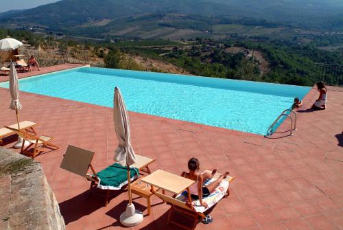 a woman sitting in chairs next to a swimming pool at Castello Vicchiomaggio in Greve in Chianti