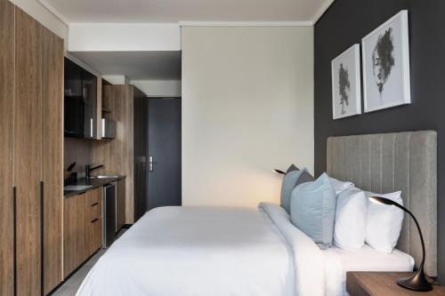 a bedroom with a large white bed and a kitchen at The Capital Trilogy Menlyn Maine in Pretoria