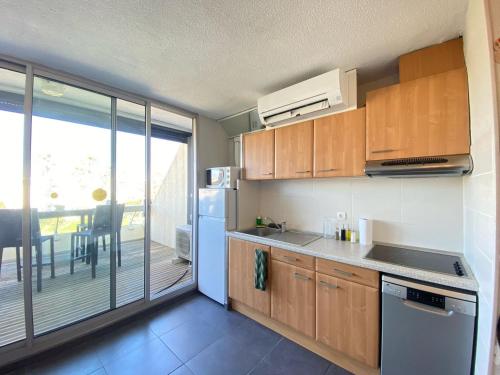une cuisine avec des placards en bois et une vue sur un balcon. dans l'établissement L'Escale d'Héliopolis, Climatisé, Coeur du village, au Cap d'Agde
